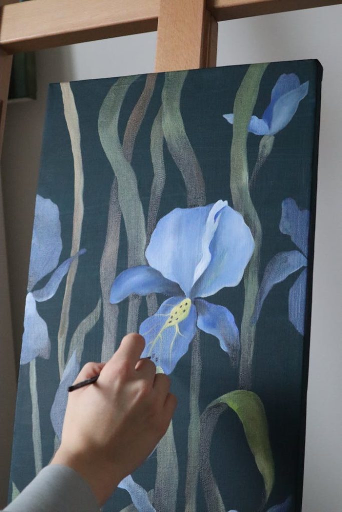 Close-up of hand painting blue irises on canvas, showcasing artistic expression.